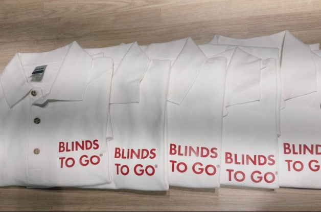 A row of white Blinds To Go branded polo shirts from a production run