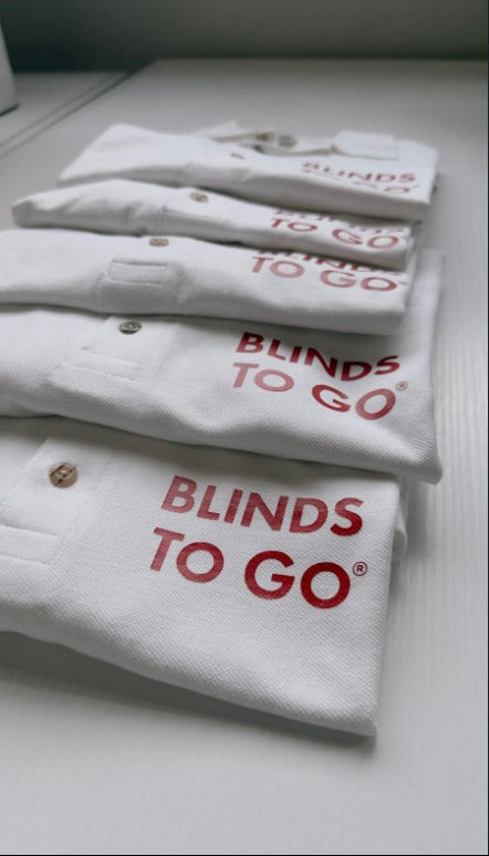 Folded white polo shirts printed with the Blinds To Go logo
